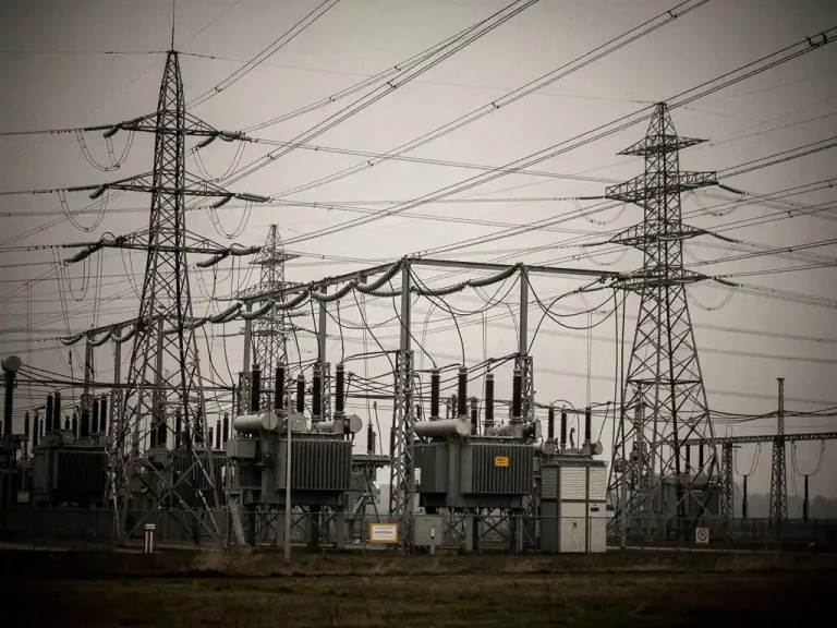 Overbelast Nederlands elektriciteitsstation met hoogspanningsmasten en transformatoren in een vlak polderlandschap onder bewolkte lucht.