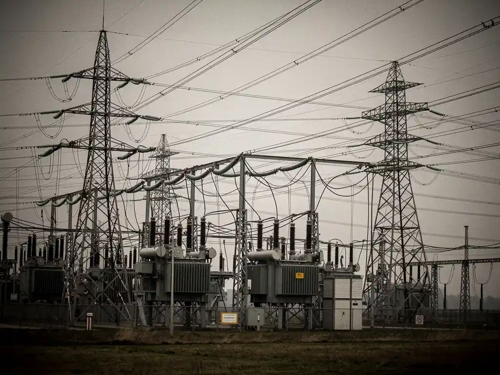 Overbelast Nederlands elektriciteitsstation met hoogspanningsmasten en transformatoren in een vlak polderlandschap onder bewolkte lucht.